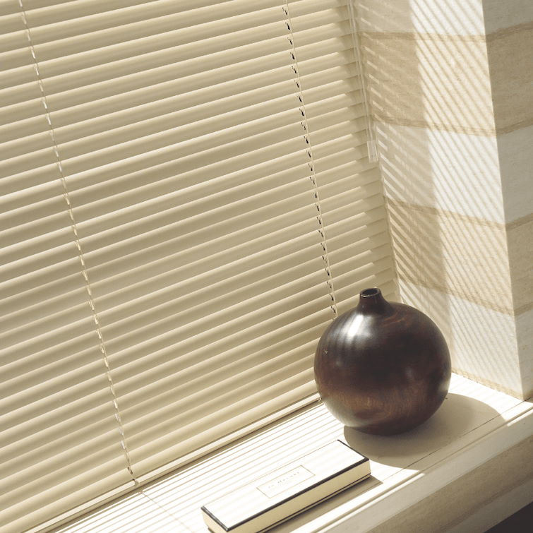 a close up image of Aluminium venetian blinds next to window ledge with an brown ornament on top of it 