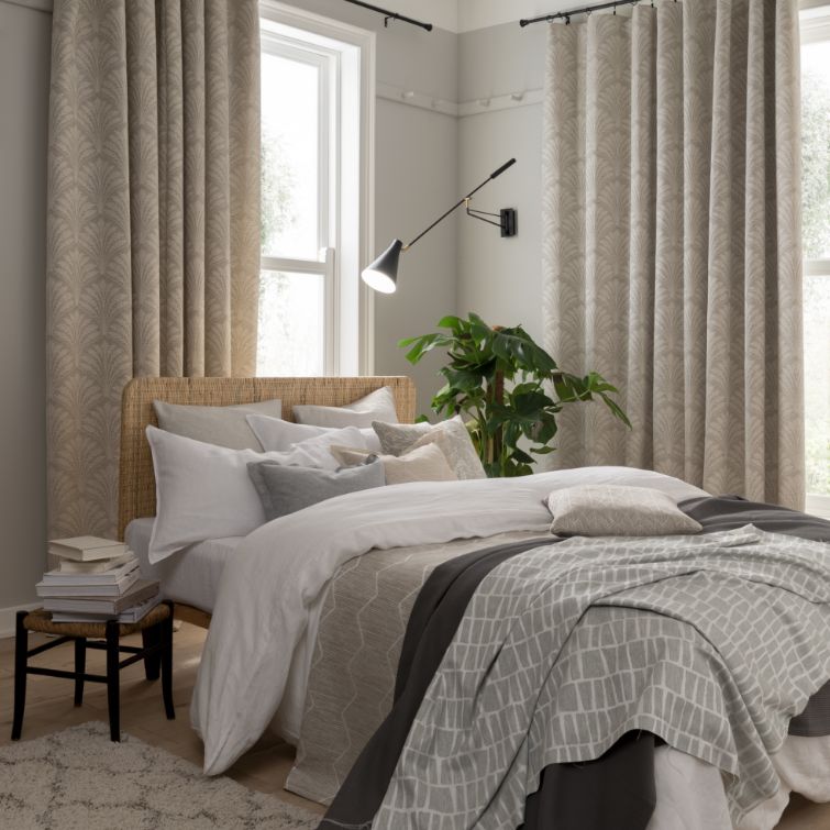 bedroom room set image with two windows with curtains and a bed next to house plant and lamp shade 