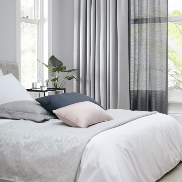 close up photo of bed next to two windows with grey and voile bedroom curtains