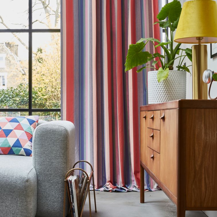 photo of colourful eyelet curtains next to wooden cabinet and grey sofa 
