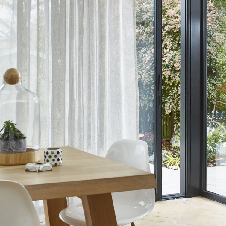 image of wooden table in kitchen next to open patio door with voile curtains 