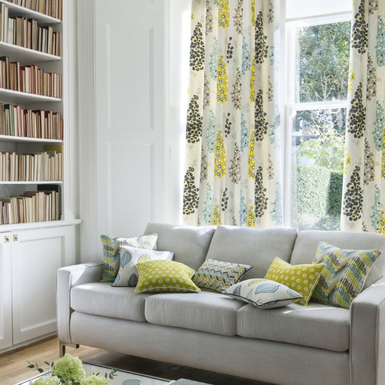 Image of living room with grey sofa infront of windows with floral curtains 
