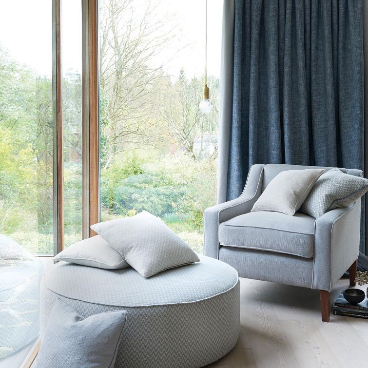 close up image of grey chair and foot rest infront of large window and dark blue living room curtains 