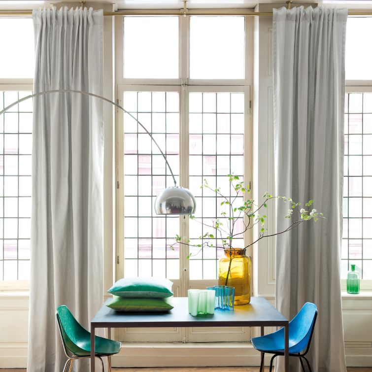 image of table with colourful chairs next to window with pencil pleat curtains installed 