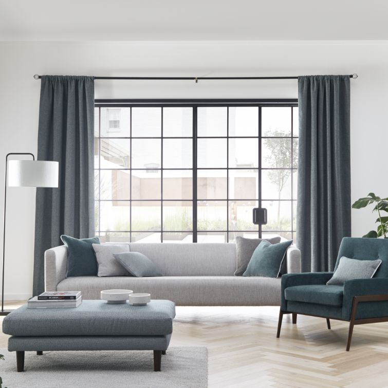 room set image of blue and grey themed living room with large windows and blue pencil pleat curtains 