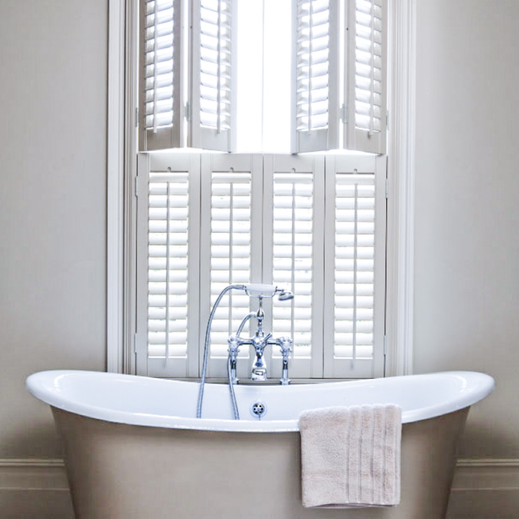 a photo of bath tub underneath window with shutters attached to it